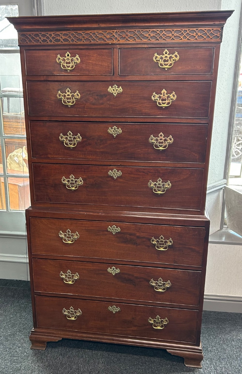 A tall Georgian mahogany chest on chest featuring eight drawers with brass swan-neck handles, blind fretwork frieze, and bracket feet.