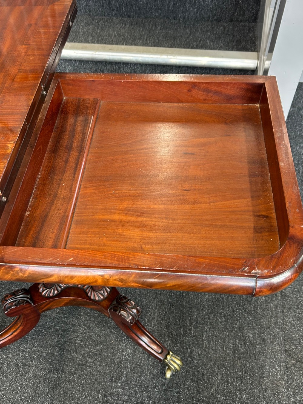 A William IV mahogany fold-over tea table with a flame mahogany top, central carved pedestal, and four splayed legs with brass paw castors. View V
