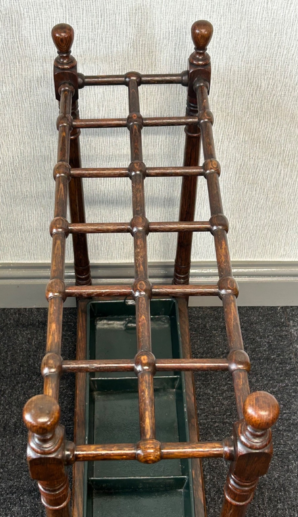 A dark oak stick stand featuring a multi-section top grid, four turned corner posts with finials, and a removable dark metal drip tray. View III