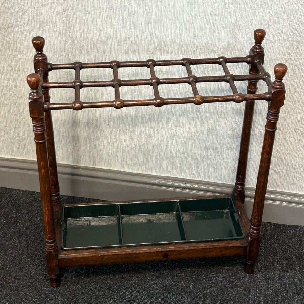 A dark oak stick stand featuring a multi-section top grid, four turned corner posts with finials, and a removable dark metal drip tray. View IV
