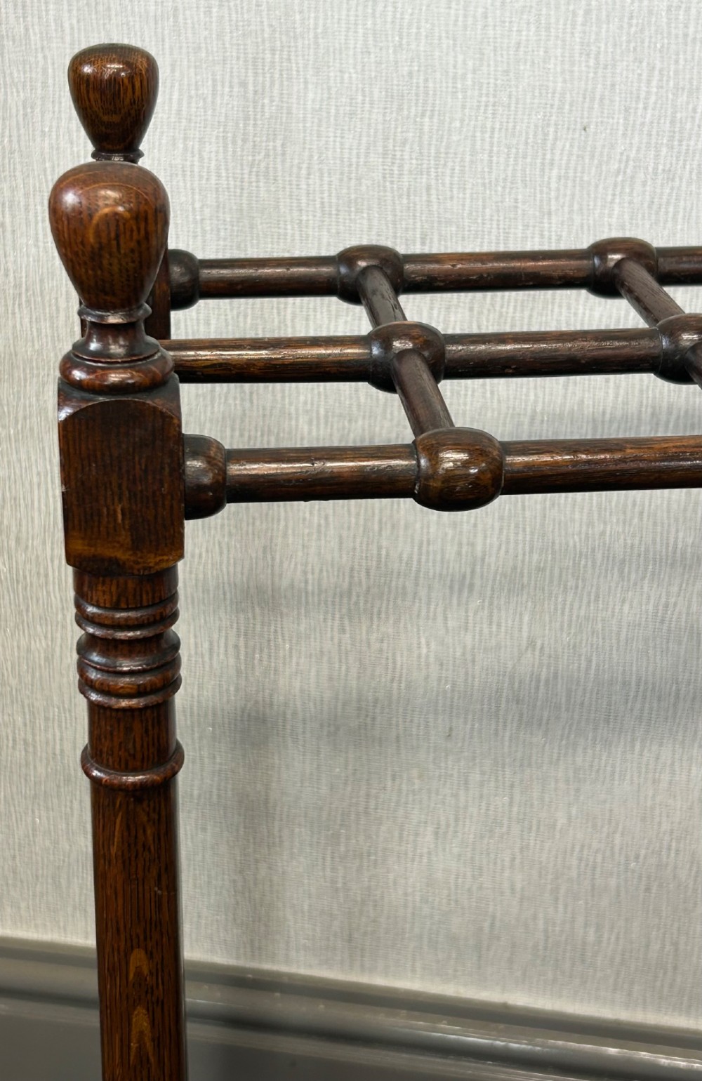 A dark oak stick stand featuring a multi-section top grid, four turned corner posts with finials, and a removable dark metal drip tray. View V