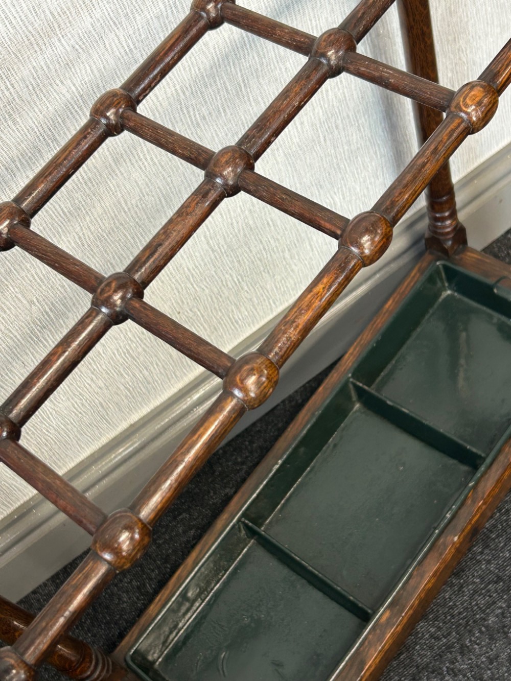 A dark oak stick stand featuring a multi-section top grid, four turned corner posts with finials, and a removable dark metal drip tray. View VI