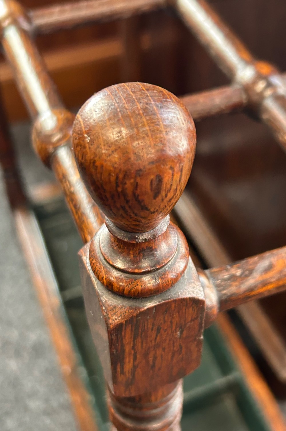 A dark oak stick stand featuring a multi-section top grid, four turned corner posts with finials, and a removable dark metal drip tray. View VII