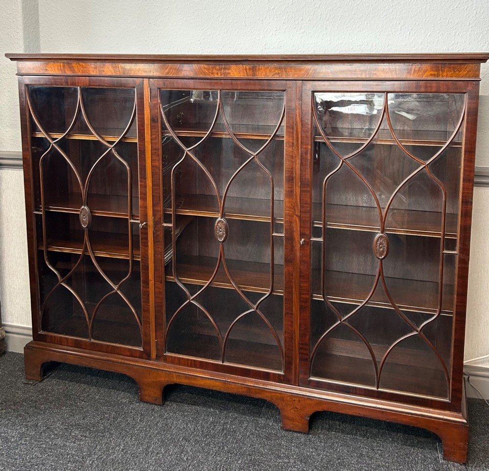 A large mahogany three-door glazed bookcase featuring geometric astragal glazing bars, carved oval motifs, and bracket feet.
