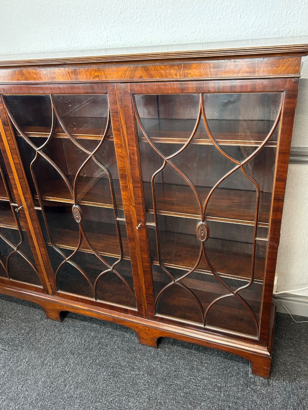 A large mahogany three-door glazed bookcase featuring geometric astragal glazing bars, carved oval motifs, and bracket feet. View III