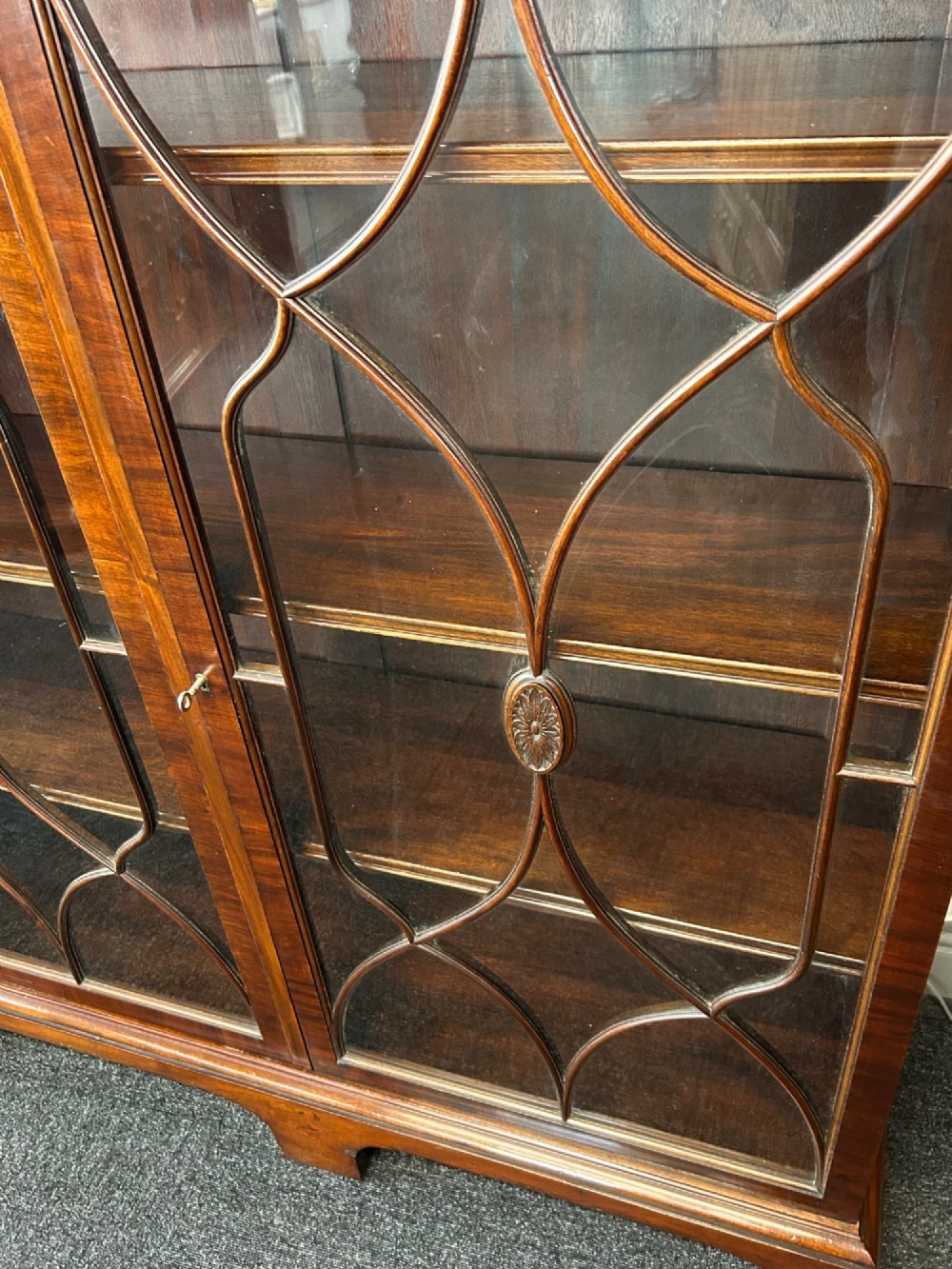 A large mahogany three-door glazed bookcase featuring geometric astragal glazing bars, carved oval motifs, and bracket feet. View IV