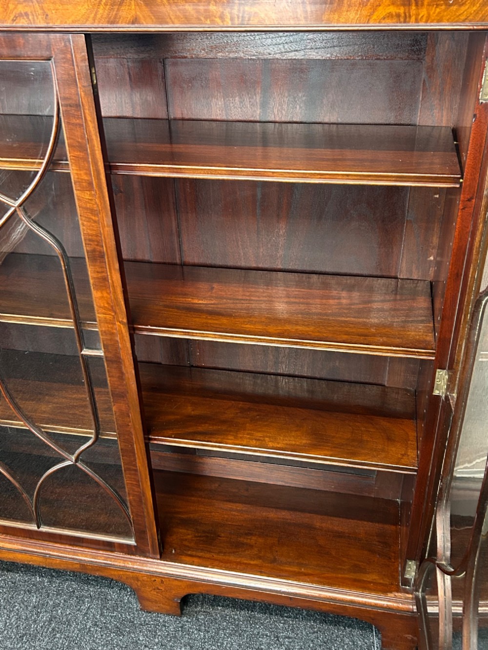 A large mahogany three-door glazed bookcase featuring geometric astragal glazing bars, carved oval motifs, and bracket feet. View V