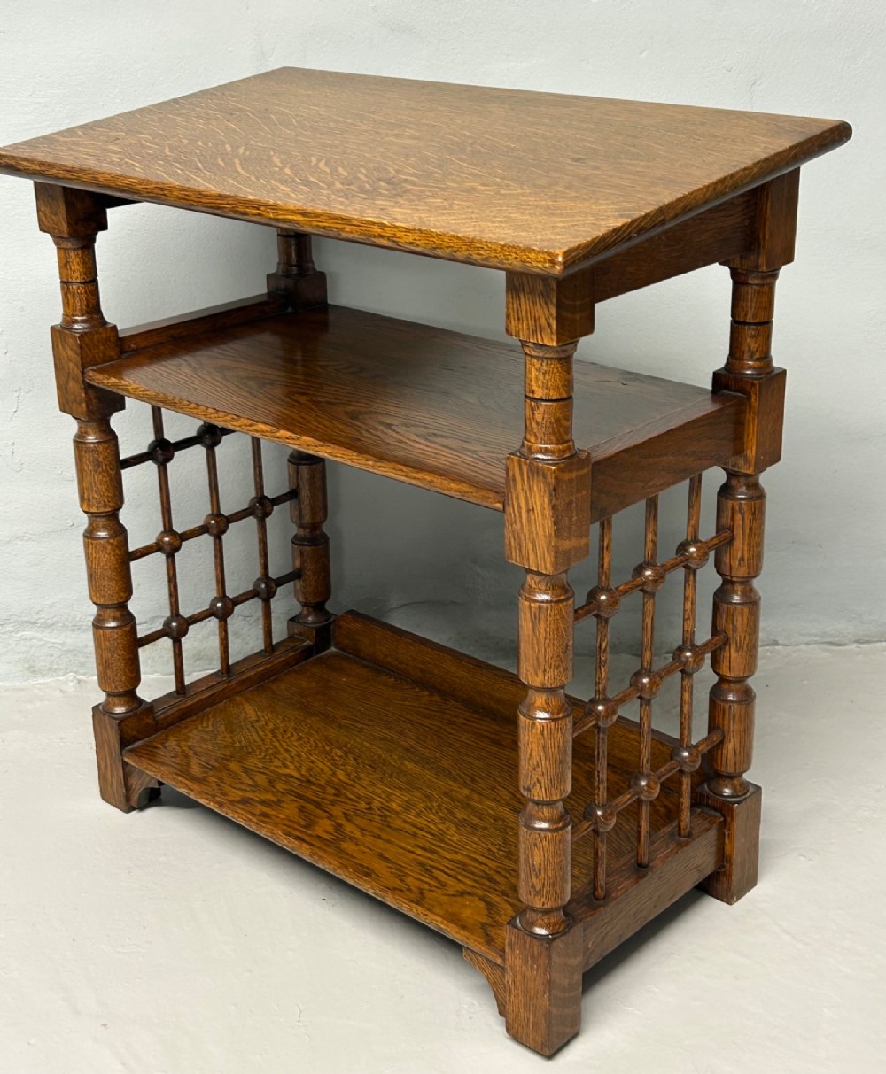An antique warm brown oak book stand featuring a slanted top reading surface, two lower shelves, and turned spindle side galleries.