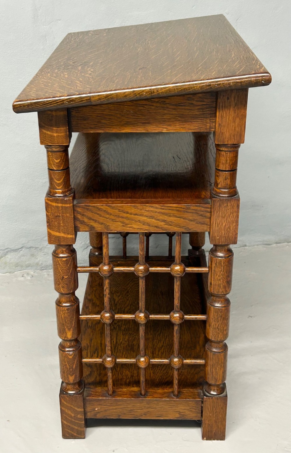 An antique warm brown oak book stand featuring a slanted top reading surface, two lower shelves, and turned spindle side galleries. View III