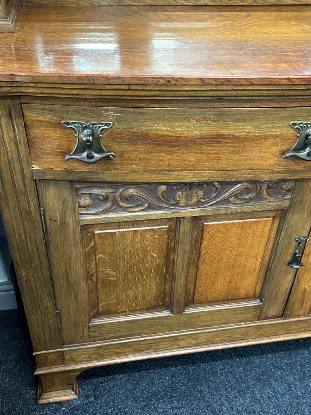 An Edwardian Arts and Crafts oak sideboard featuring a central mirrored superstructure flanked by bow-fronted leaded glass cabinets above drawers and carved panel doors. View III