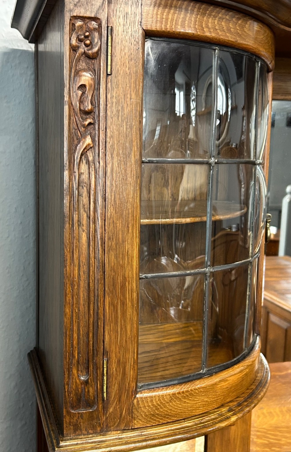 An Edwardian Arts and Crafts oak sideboard featuring a central mirrored superstructure flanked by bow-fronted leaded glass cabinets above drawers and carved panel doors. View VI