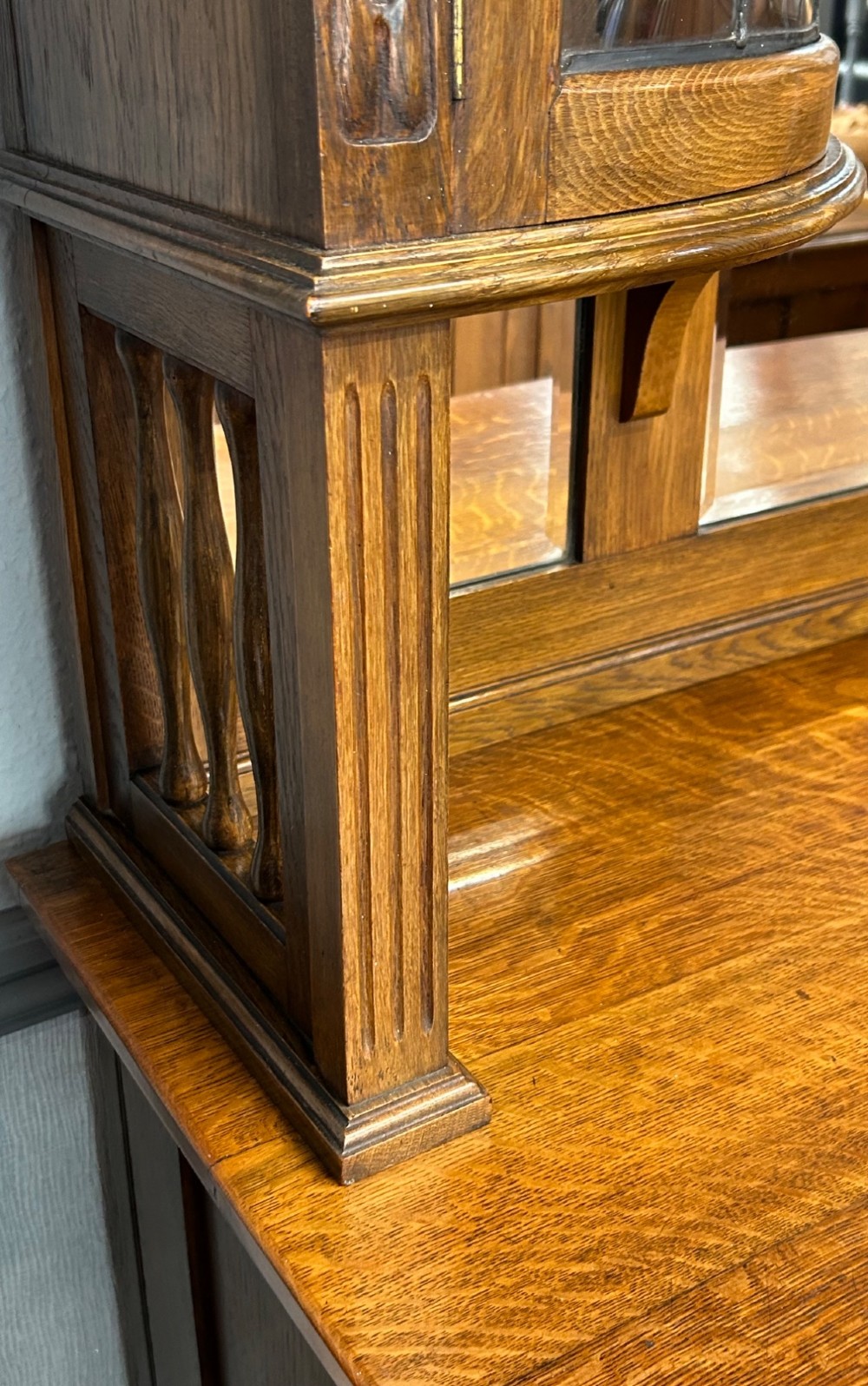 An Edwardian Arts and Crafts oak sideboard featuring a central mirrored superstructure flanked by bow-fronted leaded glass cabinets above drawers and carved panel doors. View VII