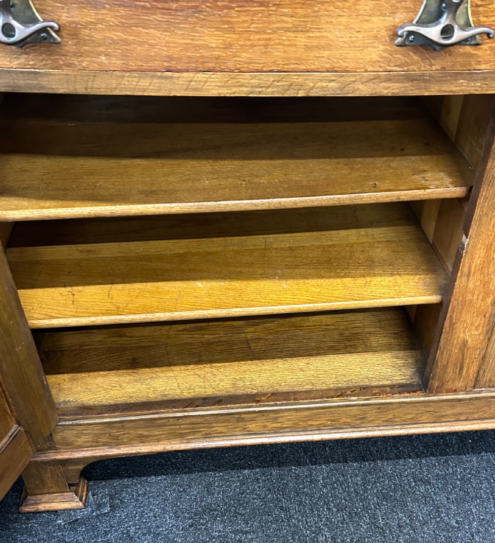 An Edwardian Arts and Crafts oak sideboard featuring a central mirrored superstructure flanked by bow-fronted leaded glass cabinets above drawers and carved panel doors. View IX