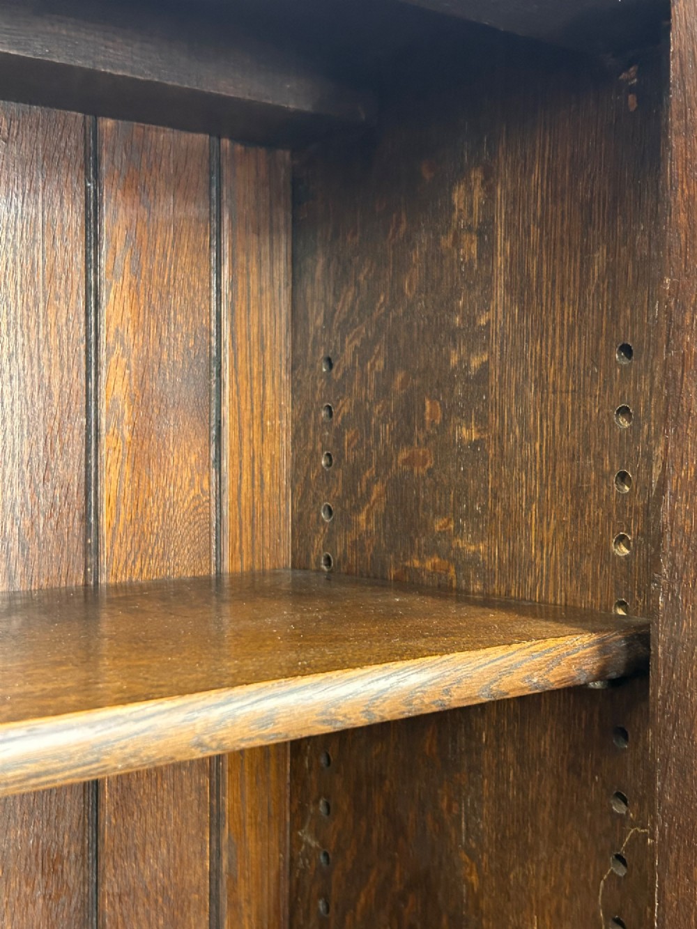 A medium brown oak cabinet featuring two glass-panelled doors, internal wooden shelves, a carved decorative apron, and turned legs with connecting stretchers. View V