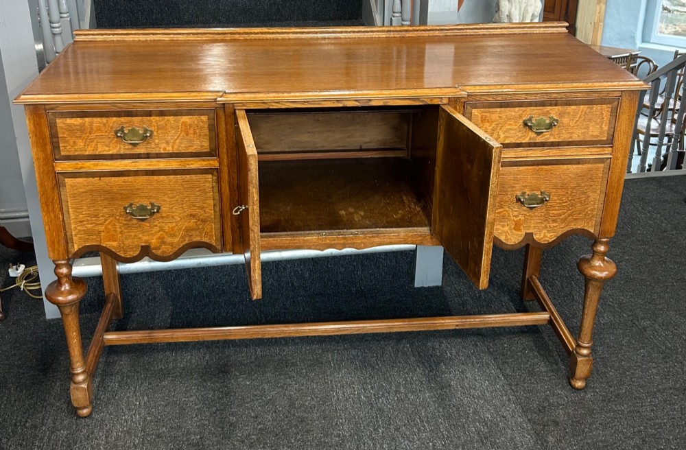 An antique oak sideboard featuring central burr walnut cupboard doors, four side drawers, brass drop handles, shaped aprons, and turned legs with a stretcher base. View III