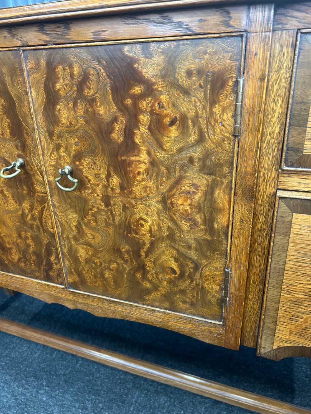 An antique oak sideboard featuring central burr walnut cupboard doors, four side drawers, brass drop handles, shaped aprons, and turned legs with a stretcher base. View V