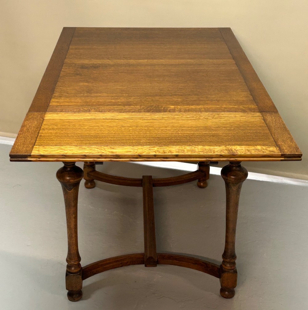 A medium brown oak draw-leaf extending dining table featuring turned baluster legs joined by a curved stretcher base. View II