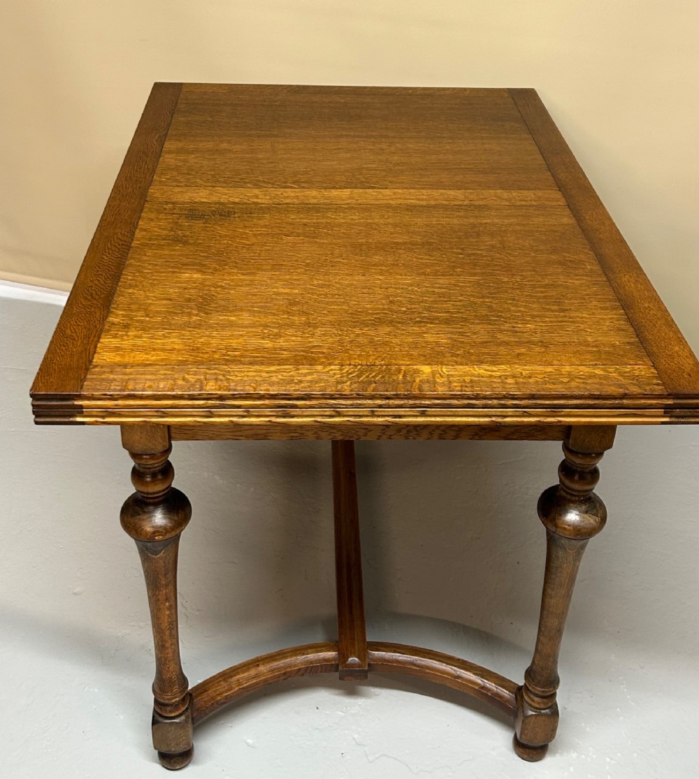 A medium brown oak draw-leaf extending dining table featuring turned baluster legs joined by a curved stretcher base. View III