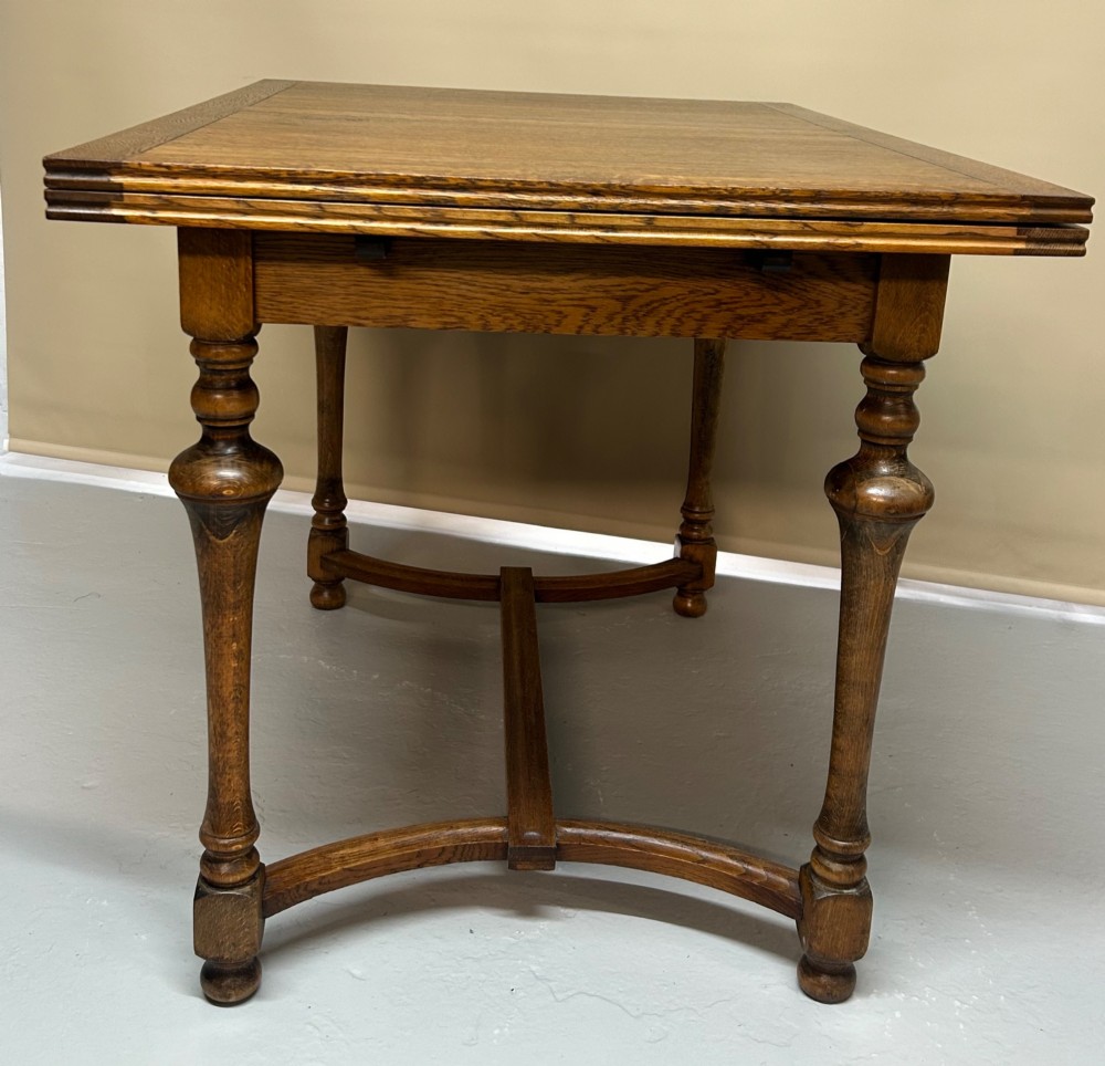A medium brown oak draw-leaf extending dining table featuring turned baluster legs joined by a curved stretcher base. View IV