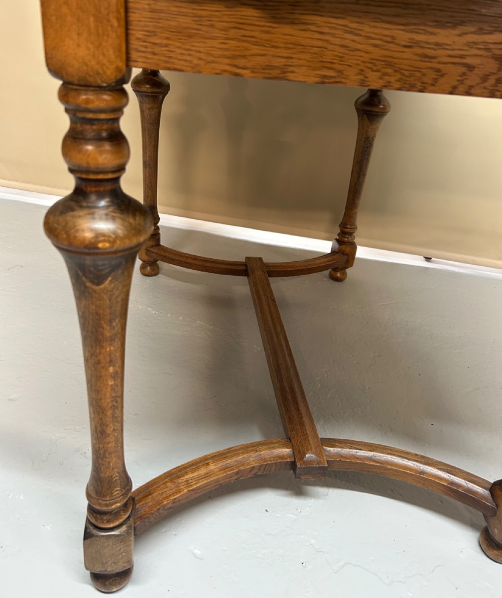A medium brown oak draw-leaf extending dining table featuring turned baluster legs joined by a curved stretcher base. View V