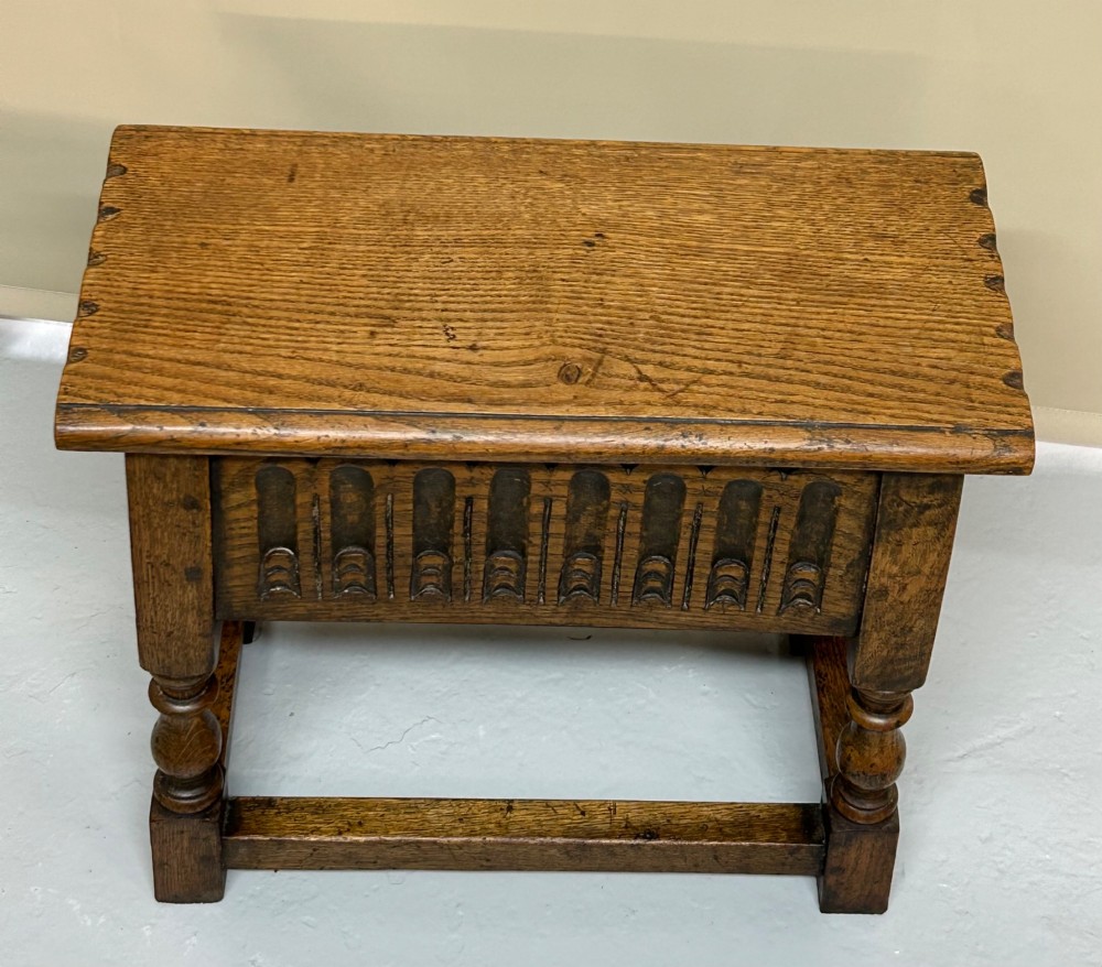 A solid oak Jacobean style box stool featuring a carved decorative apron, turned legs, lower stretchers, and a flat hinged top.