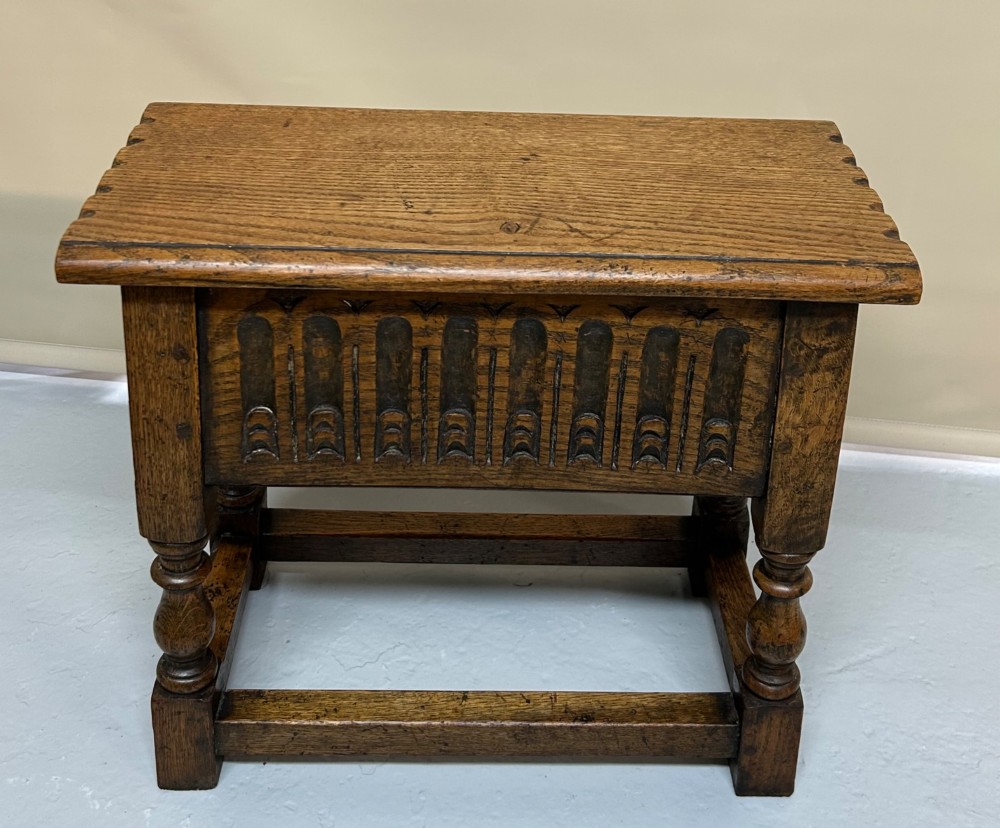 A solid oak Jacobean style box stool featuring a carved decorative apron, turned legs, lower stretchers, and a flat hinged top. View II