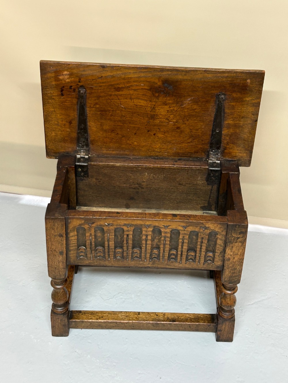 A solid oak Jacobean style box stool featuring a carved decorative apron, turned legs, lower stretchers, and a flat hinged top. View III