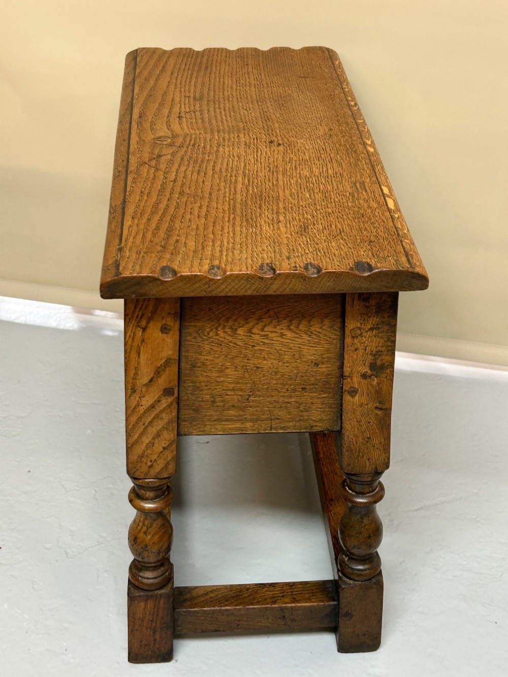A solid oak Jacobean style box stool featuring a carved decorative apron, turned legs, lower stretchers, and a flat hinged top. View IV