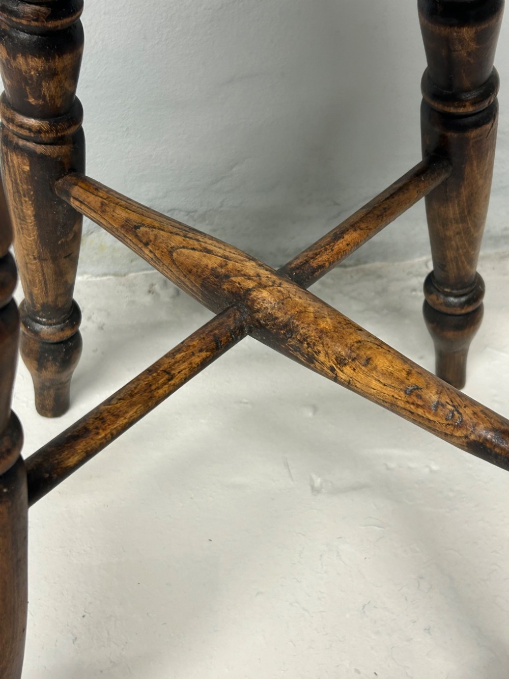 An antique wooden tavern stool with a circular dished elm seat, four turned beech legs, and cross stretchers in a warm brown timber finish. View IV