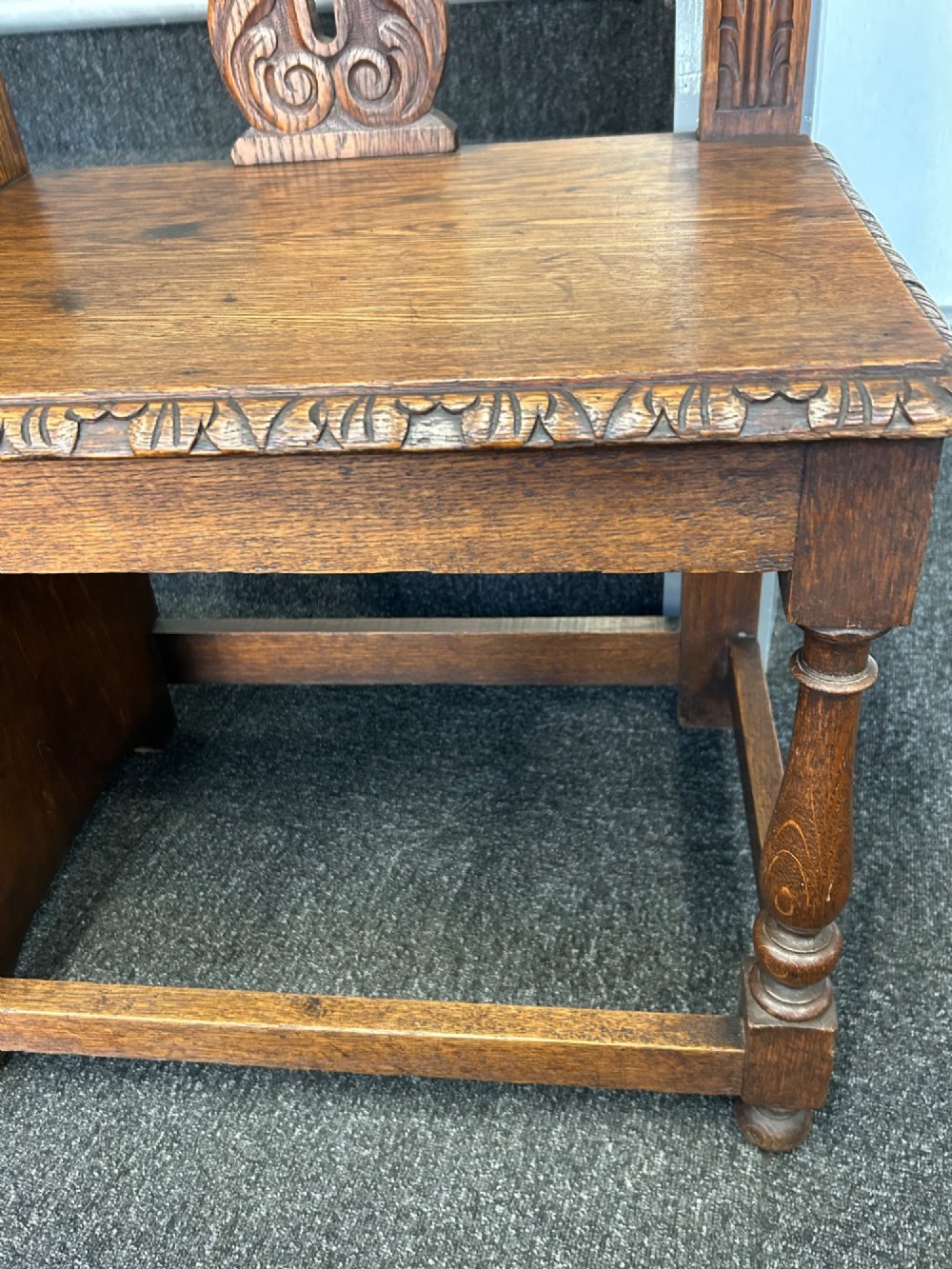 An antique carved oak hall seat featuring an integrated umbrella stand with drip tray, side shelf, and carved foliate back panels topped with a shell pediment. View VI
