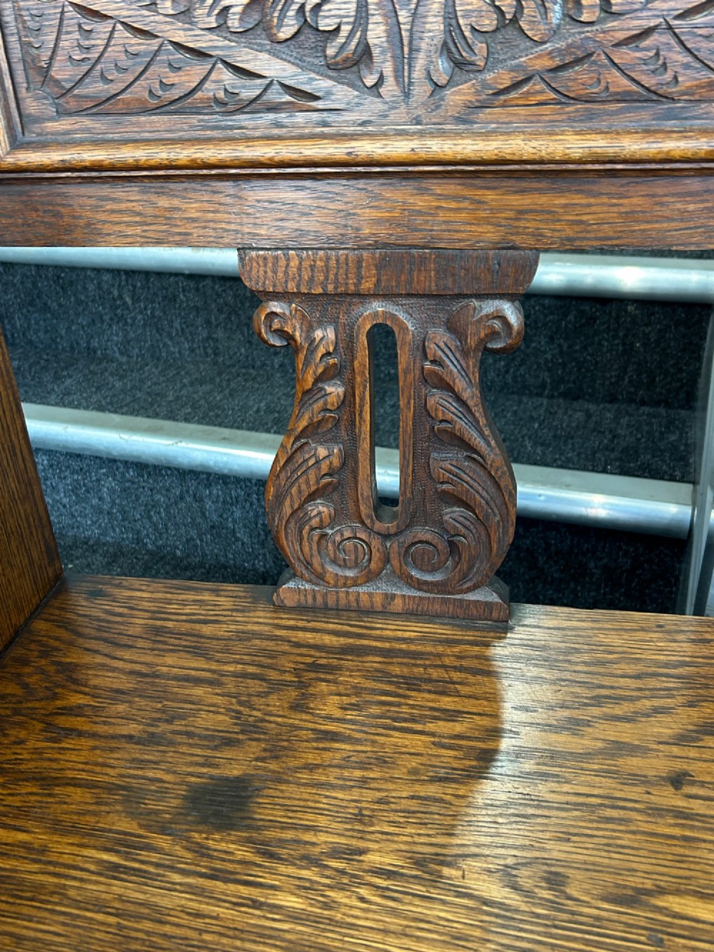 An antique carved oak hall seat featuring an integrated umbrella stand with drip tray, side shelf, and carved foliate back panels topped with a shell pediment. View VII