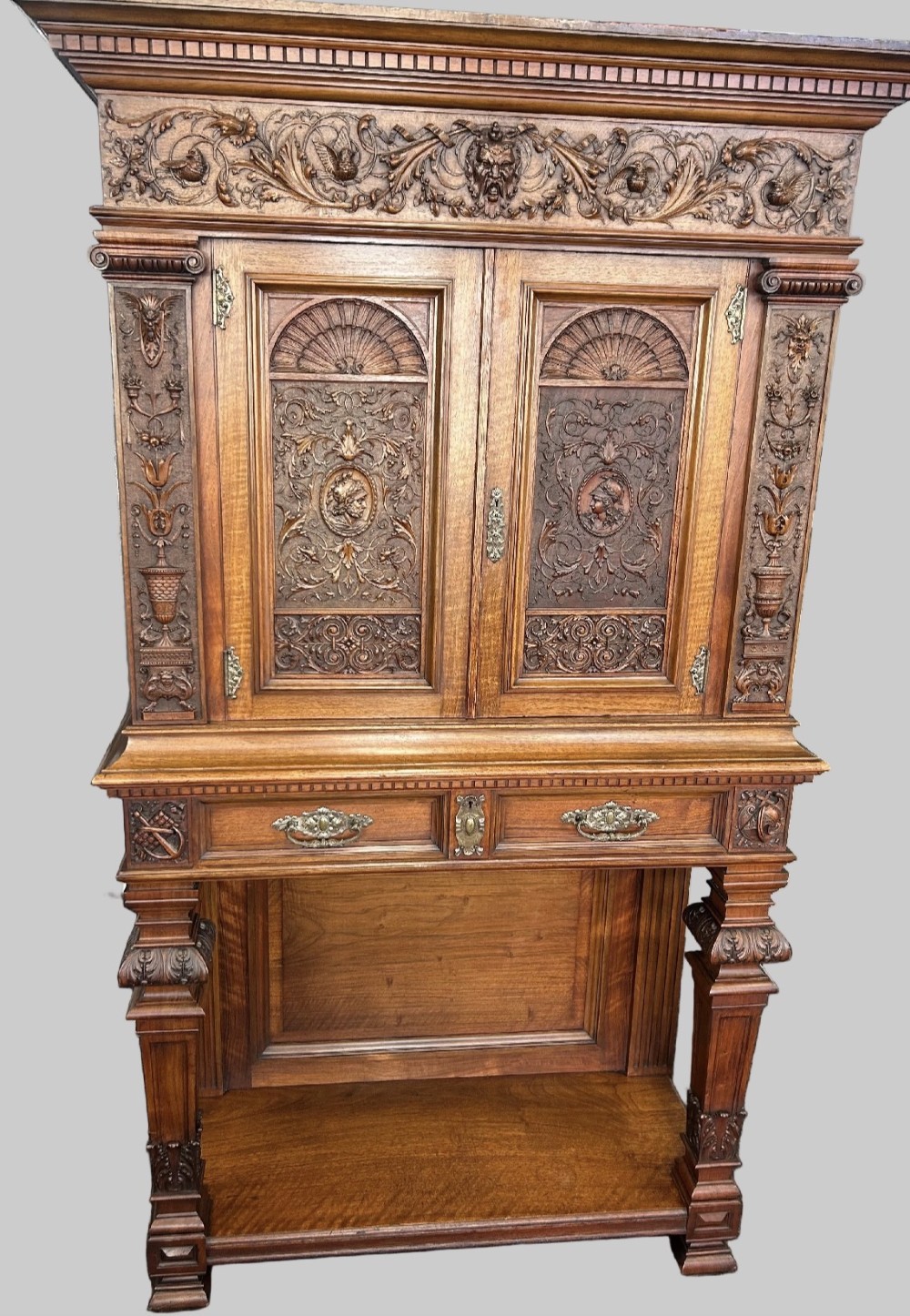 A 19th-century Renaissance Revival carved wood cabinet-on-stand with intricate relief carvings, twin doors, upper drawers, and an open lower shelf.