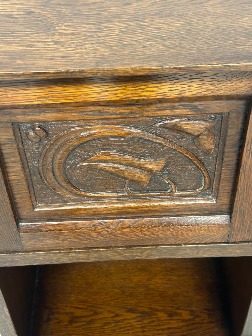 An Arts and Crafts dark oak purdonium featuring stylized carved leaf panels, an upper cupboard, an open shelf, and a slanted fall-front compartment. View VI