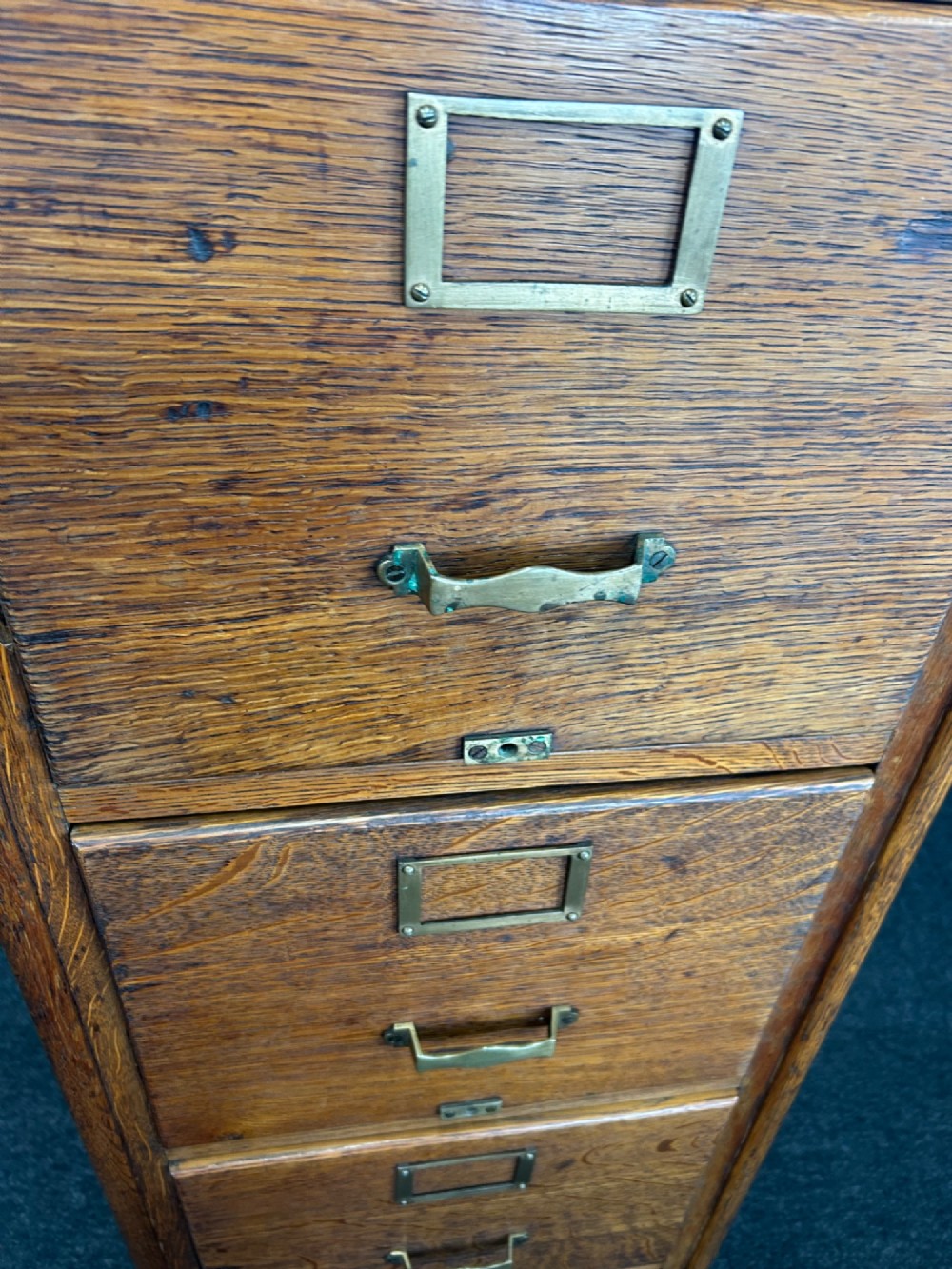 A vertical four-drawer golden oak filing cabinet featuring brass label holders and metal pull handles. View V