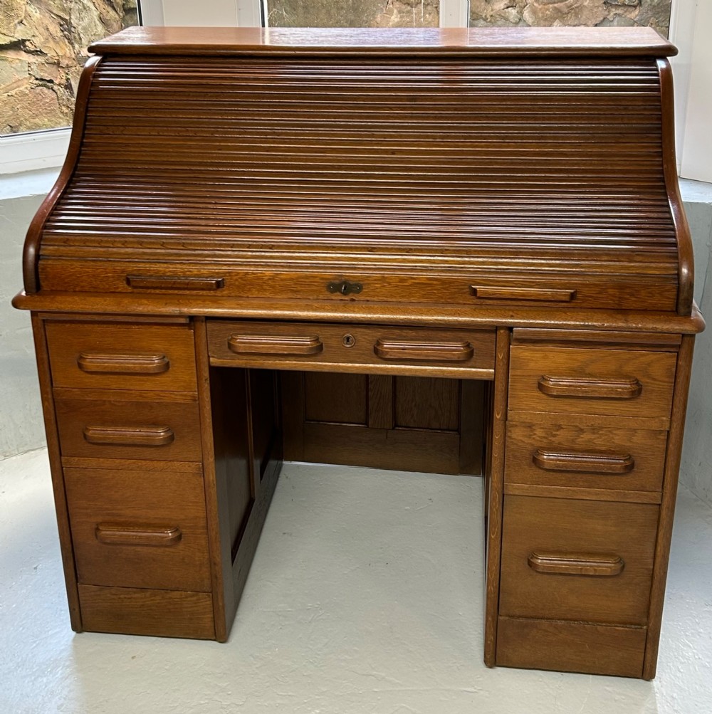 A warm brown oak roll top desk featuring a tambour slatted shutter top, central drawers, and twin pedestals with integrated storage drawers.