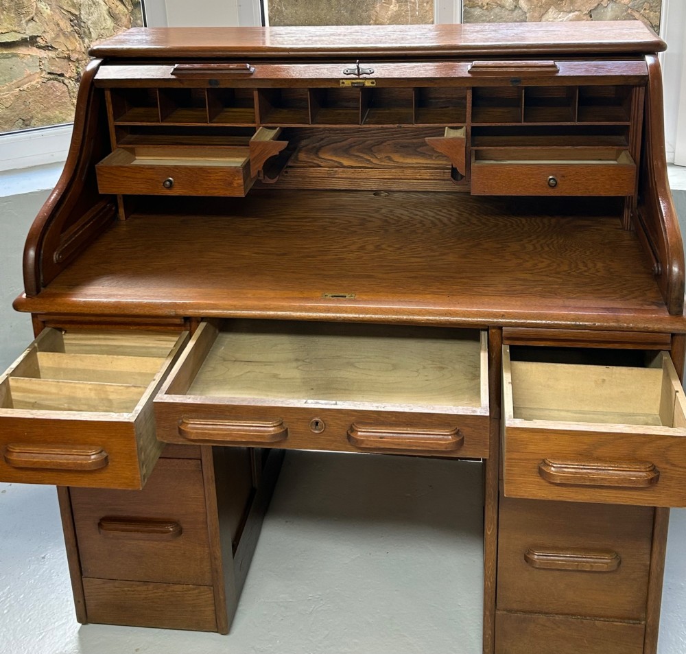 A warm brown oak roll top desk featuring a tambour slatted shutter top, central drawers, and twin pedestals with integrated storage drawers. View VI