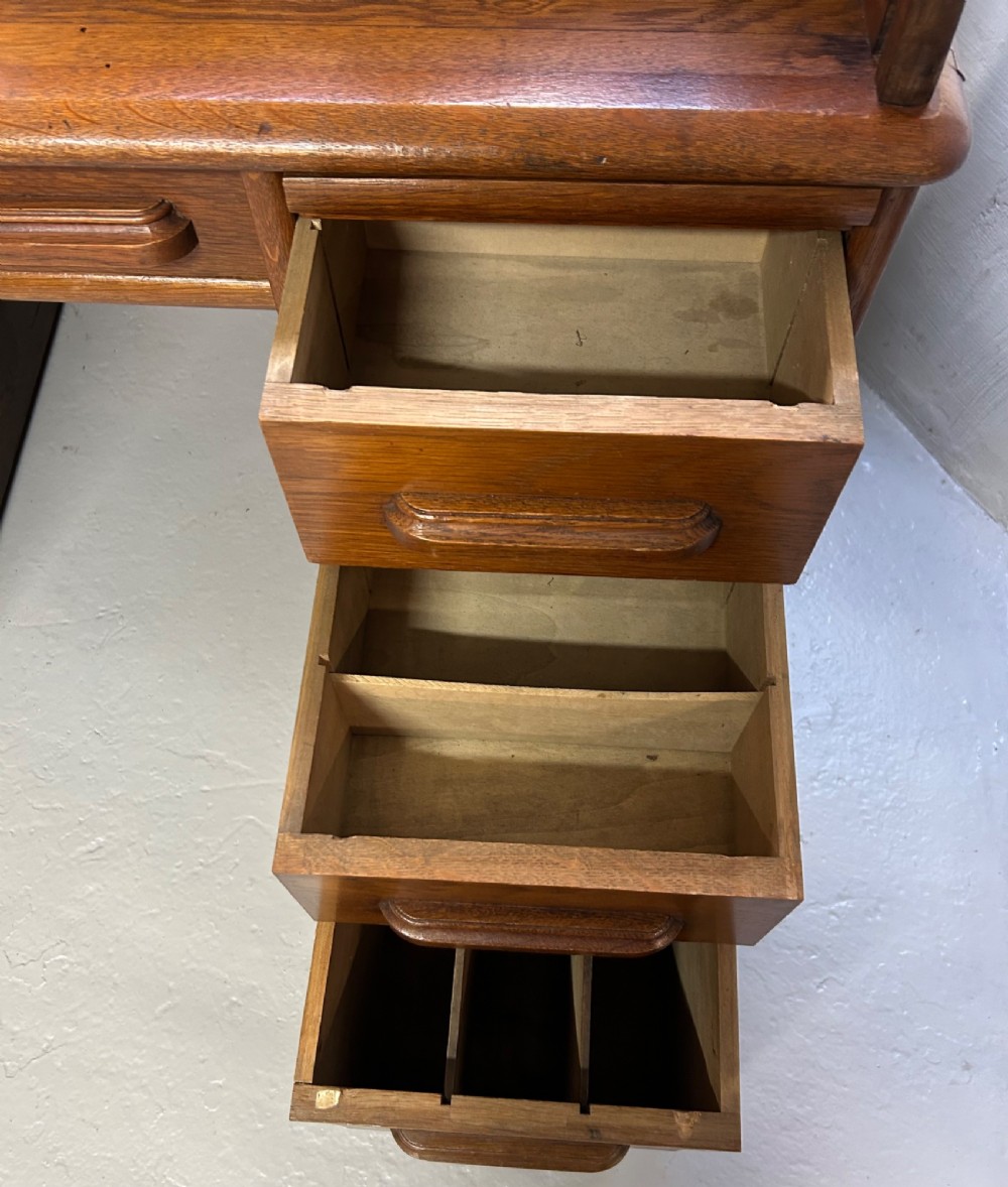 A warm brown oak roll top desk featuring a tambour slatted shutter top, central drawers, and twin pedestals with integrated storage drawers. View XI