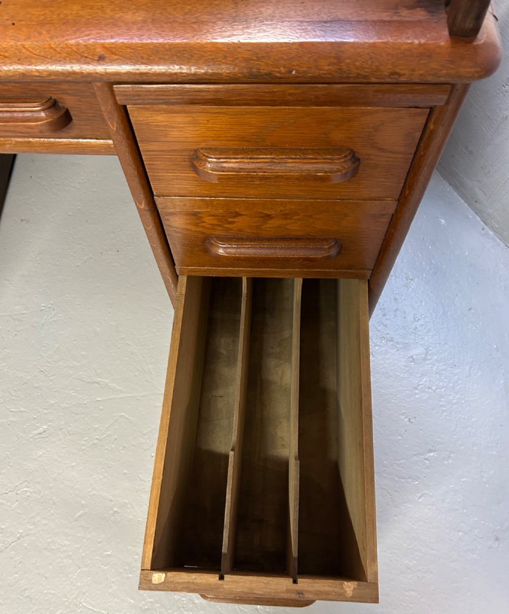 A warm brown oak roll top desk featuring a tambour slatted shutter top, central drawers, and twin pedestals with integrated storage drawers. View XII