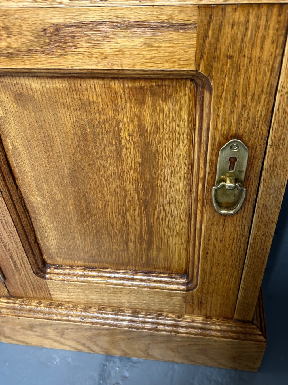 A matching pair of light oak bedside cabinets featuring carved crest galleries, single drawers, single panel doors, and brass fittings. View IV