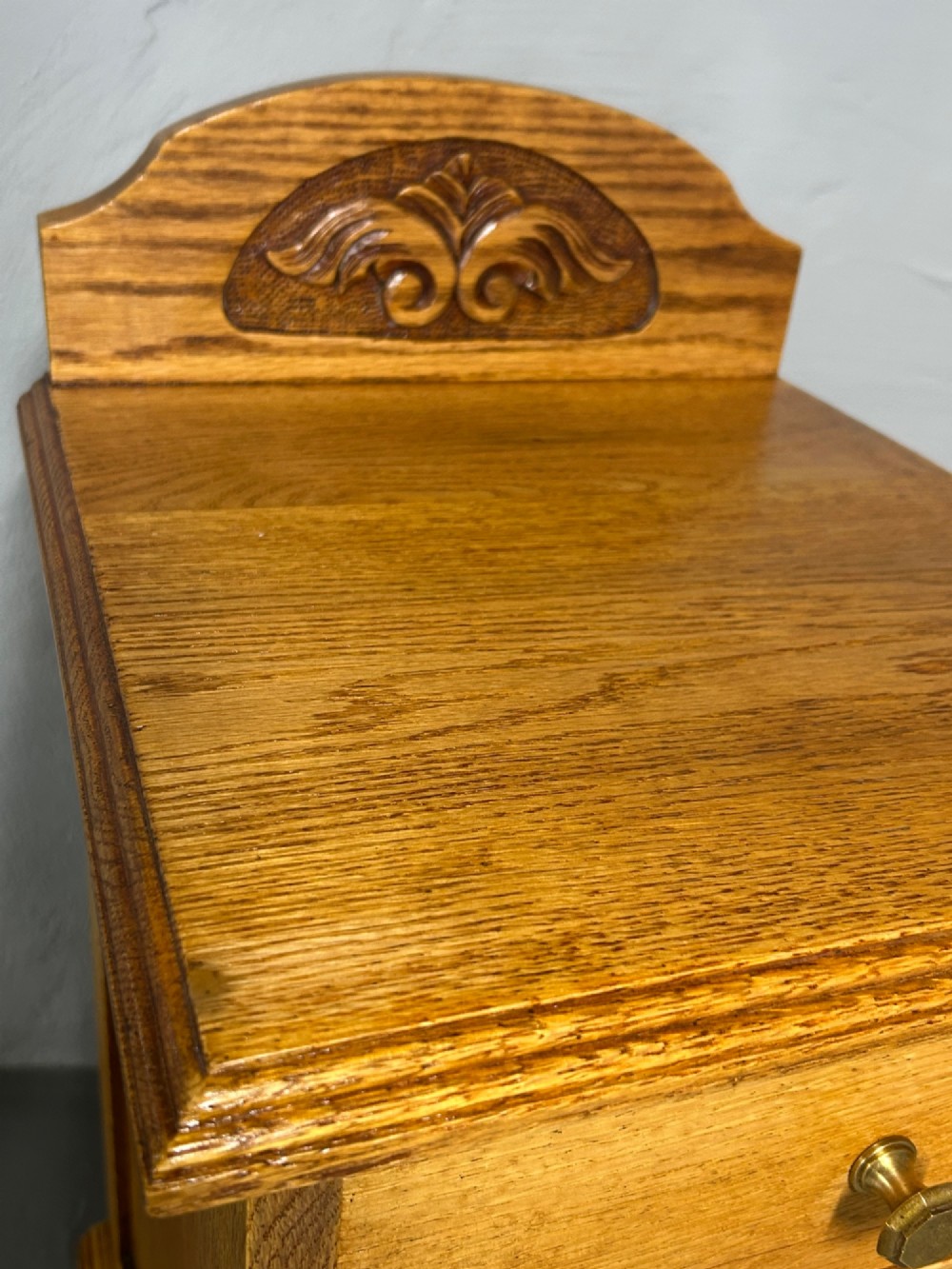 A matching pair of light oak bedside cabinets featuring carved crest galleries, single drawers, single panel doors, and brass fittings. View VI
