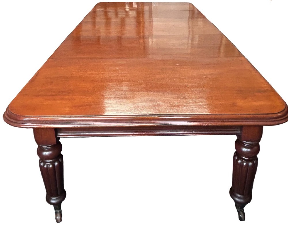 A Victorian mahogany extending dining table featuring three insertion leaves, rounded corners, polished finish, and reeded turned legs on brass castors.