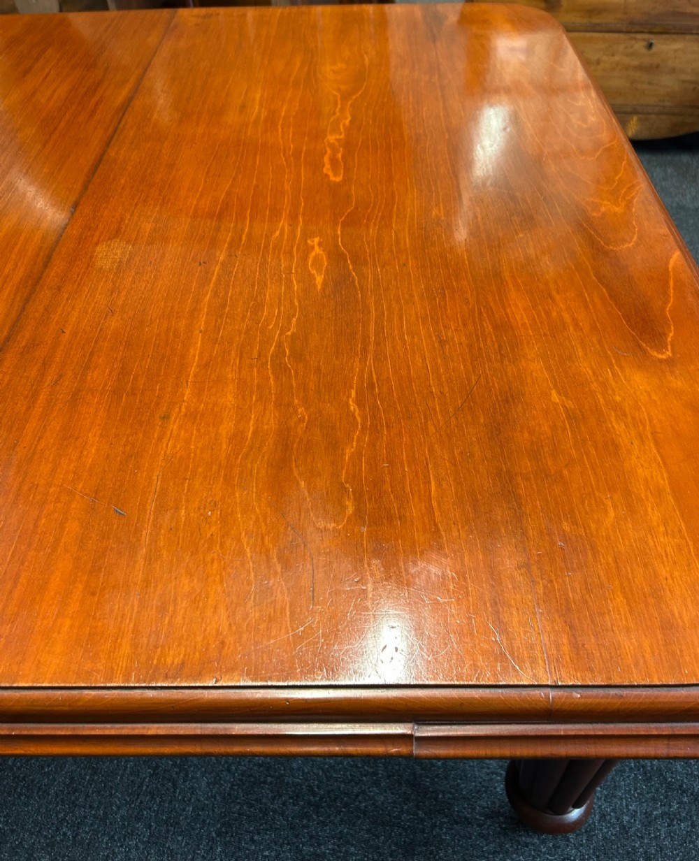 A Victorian mahogany extending dining table featuring three insertion leaves, rounded corners, polished finish, and reeded turned legs on brass castors. View VI