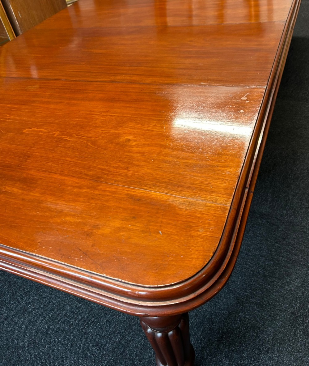 A Victorian mahogany extending dining table featuring three insertion leaves, rounded corners, polished finish, and reeded turned legs on brass castors. View VII