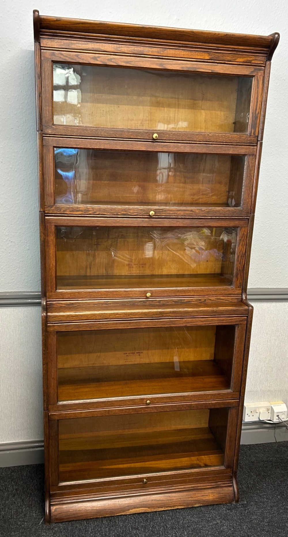 A five-tier oak barrister bookcase with glazed up-and-over doors and small brass knobs.