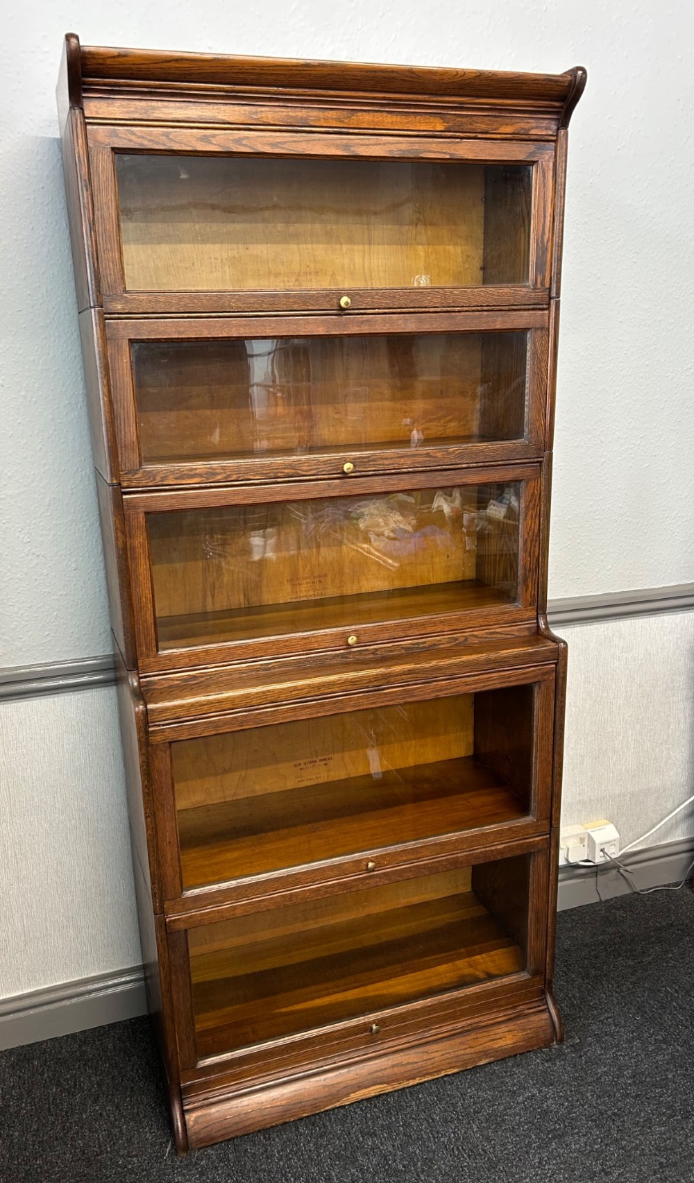 A five-tier oak barrister bookcase with glazed up-and-over doors and small brass knobs. View II