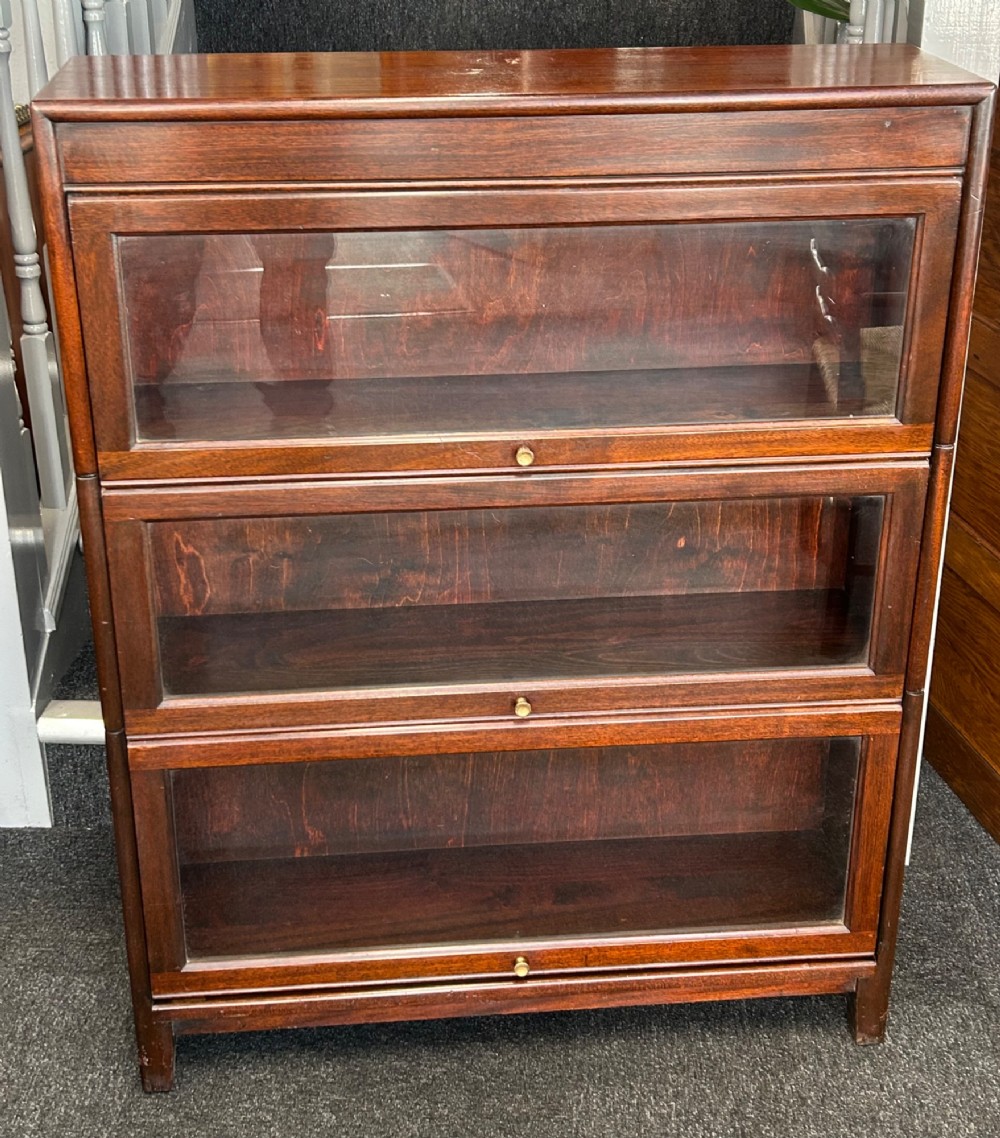 A three-tier mahogany barrister bookcase featuring glazed front doors and small circular brass knobs.