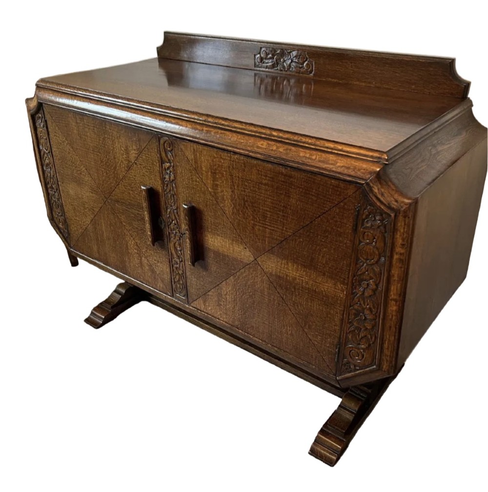 An Art Deco dark oak sideboard featuring diamond-pattern veneered double doors, carved floral borders, wooden handles, and a low upstand gallery.