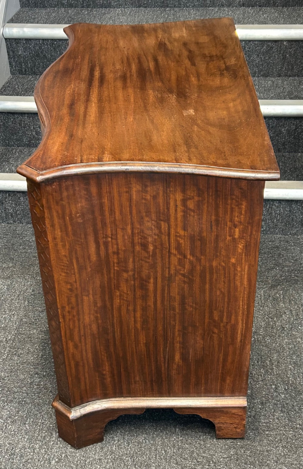 A Georgian Revival mahogany chest of drawers featuring a serpentine front, four graduated drawers with brass handles, blind fretwork on canted corners, and bracket feet. View II