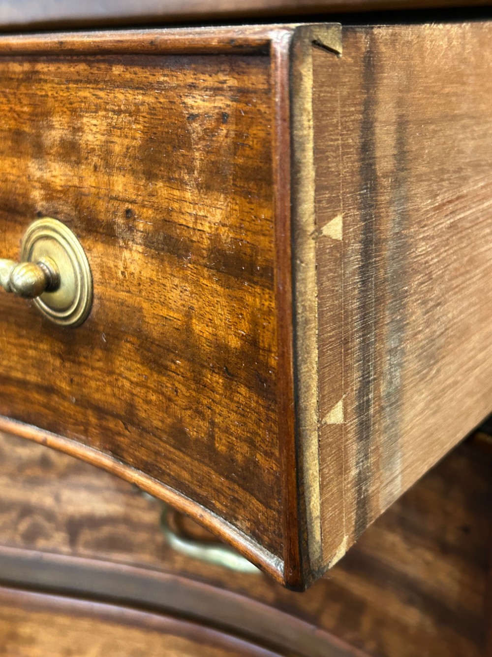 A Georgian Revival mahogany chest of drawers featuring a serpentine front, four graduated drawers with brass handles, blind fretwork on canted corners, and bracket feet. View V