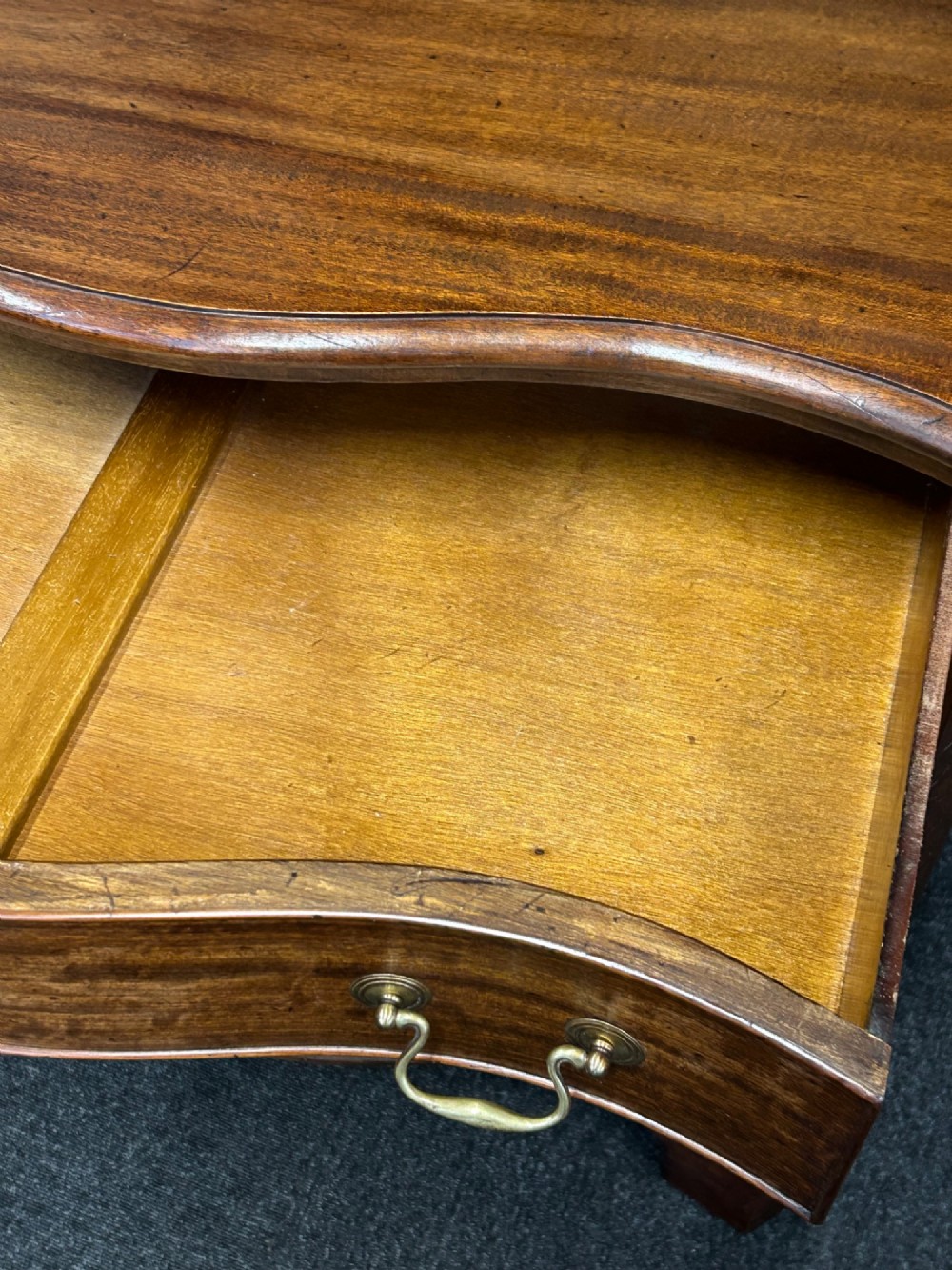 A Georgian Revival mahogany chest of drawers featuring a serpentine front, four graduated drawers with brass handles, blind fretwork on canted corners, and bracket feet. View VI
